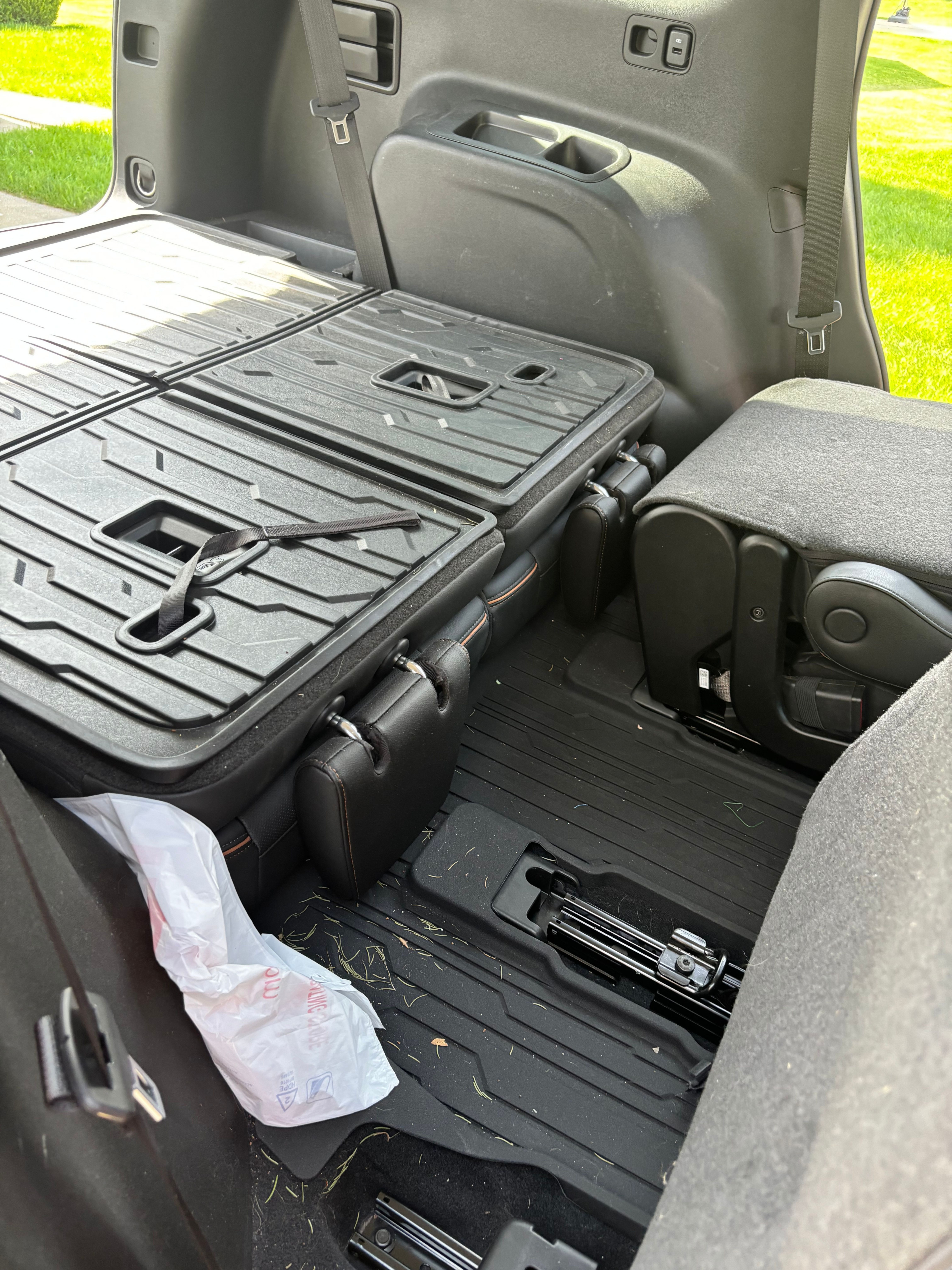 Back-row floor of a customer's SUV photographed before interior detailing — folded seat, debris and a plastic bag on the floor. An example 'show us the back row' photo for an accurate interior detailing quote.