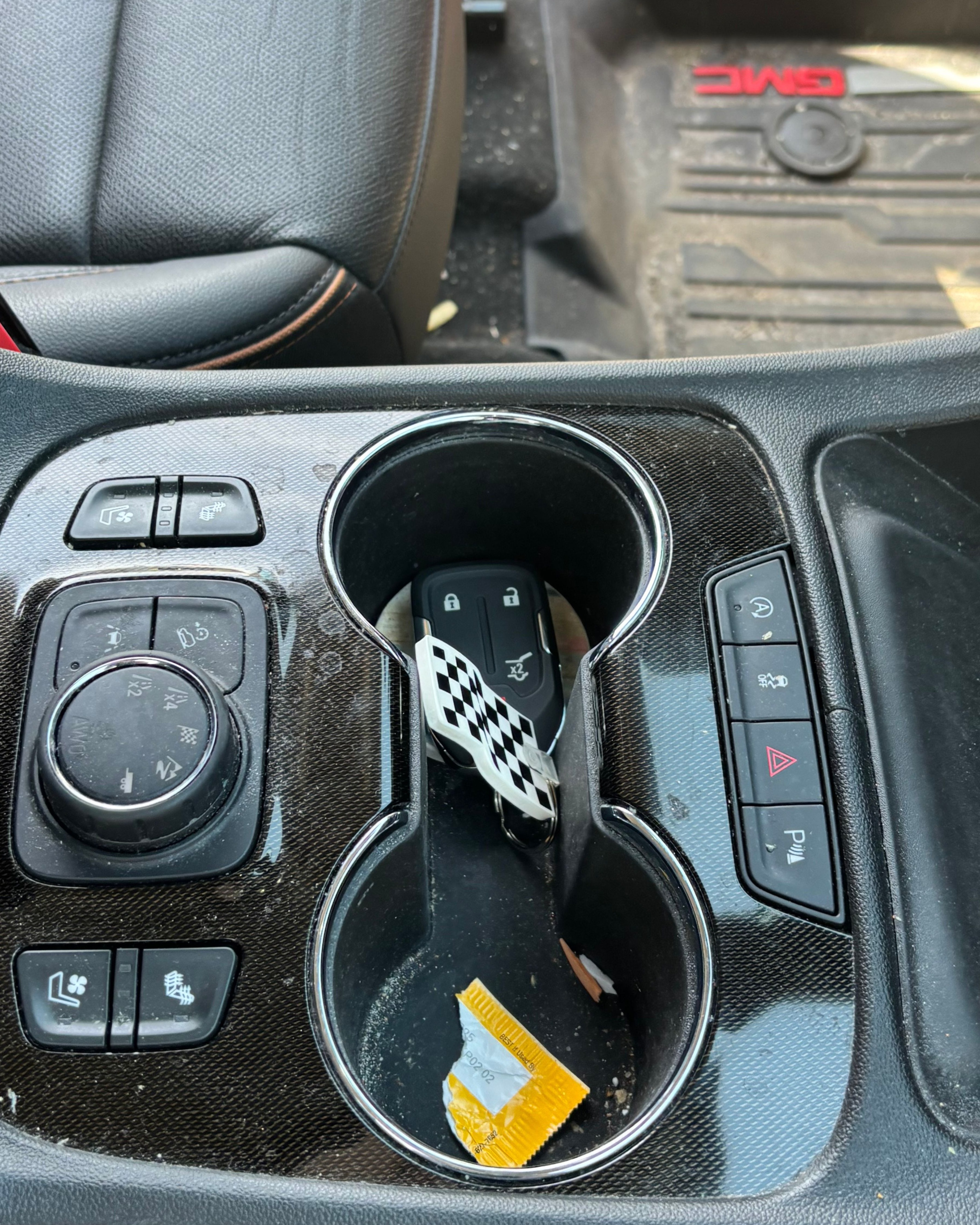 Closeup of the center console and cup holders of a customer's SUV before detailing — dust on the plastics, a wrapper in the cup holder. An example 'problem area' phone photo so we can price the toughest spots before we arrive.