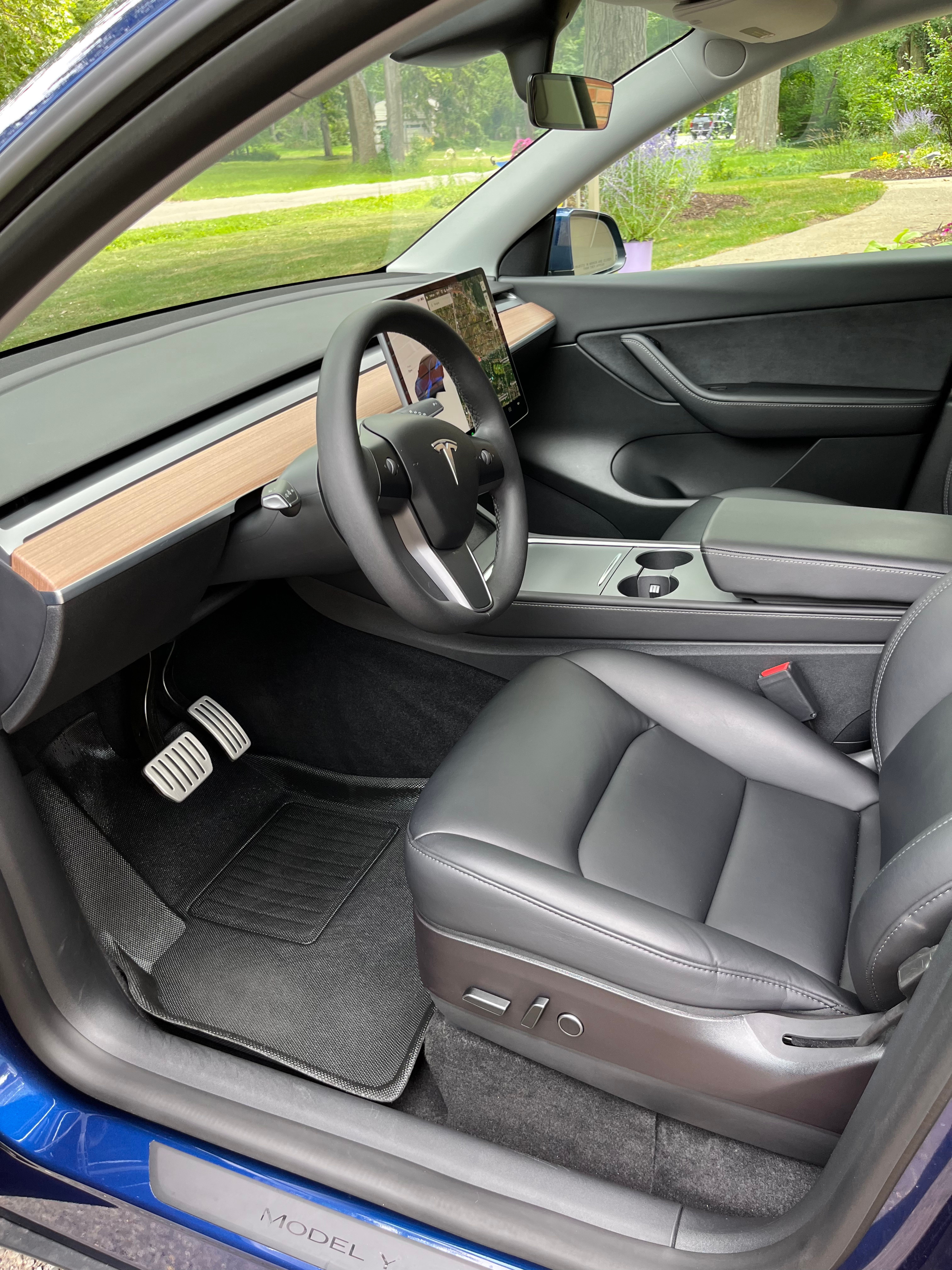 Freshly detailed Tesla Model Y interior in a Mid-Michigan driveway — wood-grain dash, matte plastic trim, and black leather seats cleaned and UV-protected to a clean, non-greasy finish. No slimy Armor-All shine, every surface conditioned.